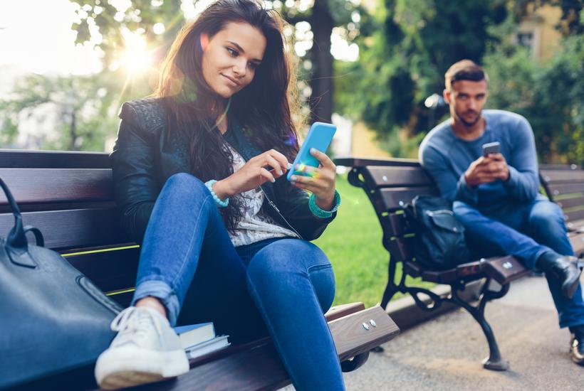 Young Couple In The Park Texting On Smartphones