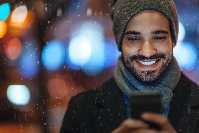 Young Man Using Smartphone On City Street On A Snowy Day